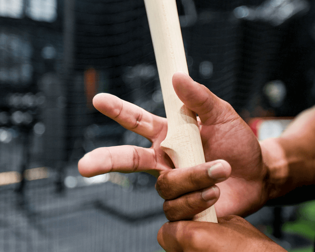 Close-up of hands holding a baseball bat with a blurred sports facility background